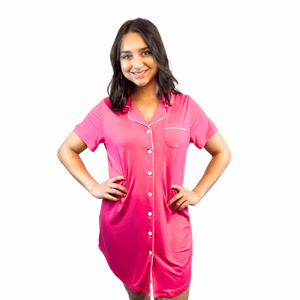 variant:fuchsia A young woman with long, dark hair wearing a bright hot pink adaptive nightgown with decorative buttons and Velcro® closures. The collar is a fold-down notched collar and the there is a breast pocket. The adaptive nightgown is trimmed in white piping. She had her hands on her hips and is smiling. 