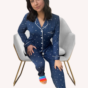 Variant::blue with hearts  A young woman with dark hair sitting on a chair, wearing navy heart bamboo long pj set.  The collar is a fold-down notched collar and the there is a breast pocket. The bamboo long pj set is trimmed in white piping.