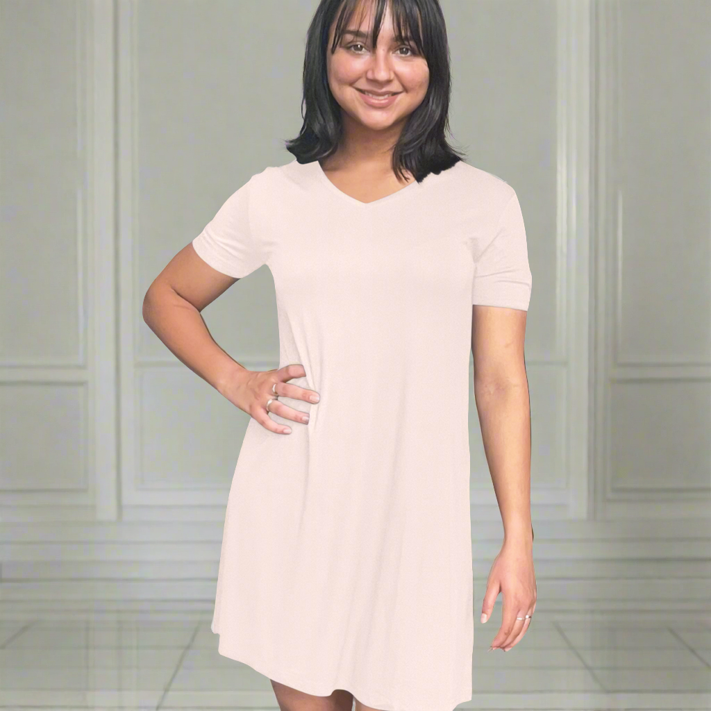 variant::pink A young woman with dark hair wearing a pink v-neck nightshirt with short sleeves that comes just above the knee. She has one hand on her hip. The fabric is Lenzing modal, a cooling fabric that is antibacterial and cooling and made from beech viscose. 