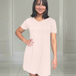 variant::pink A young woman with dark hair wearing a pink v-neck nightshirt with short sleeves that comes just above the knee. She has one hand on her hip. The fabric is Lenzing modal, a cooling fabric that is antibacterial and cooling and made from beech viscose. 