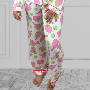 variant::preppy-pickleball A view of the legs of a young woman with dark hair wearing pink and green pickleball printed pajamas with one hand on her hip.  The collar is a fold-down notched collar and the there is a breast pocket. The bamboo long sleeve pajama set is trimmed in pink piping.