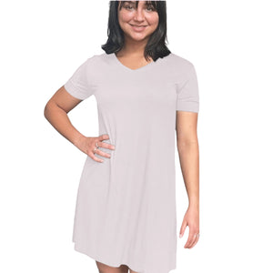 variant::pink A young woman with short hair wearing a lenzing modal v-neck gown in the color pink. She has one hand on her hip and is smiling towards the camera. There are short sleeves and the length of the nightgown comes to right above her knees.