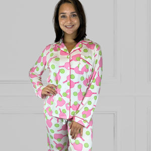variant::preppy-pickleball A front view of a  young woman with dark hair wearing pink and green pickleball printed pajamas with one hand on her hip.  The collar is a fold-down notched collar and the there is a breast pocket. The bamboo long sleeve pajama set is trimmed in pink piping.