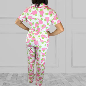 variant::preppy-pickleball Pink and green bamboo pickleball pajama set worn by young woman with dark hair. standing with her back to the camera. The background of the pajams is crisp white and the sleeves are short. The pants are cropped jogger style with a tapered leg. 
